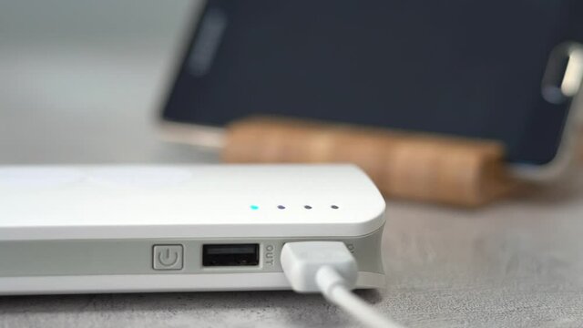 Hand turns on powerbank on background of mobile phone. External battery charges electronic devices. Flashing indicators