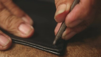 Close-up. A tailor with adult working hands punches a hole with an iron punch under rivets in collar of black leather jacket. Handmade by master with leather, hands of an old master. Slow motion. 4k. - Powered by Adobe