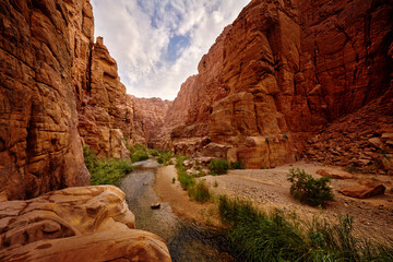 Wadi Mujib Biosphere Reserve, red rock ravine gorge with river. Jordan water stream with blue sky. Wadi Mujib lowest nature reserve landscape, with a spectacular array of scenery near Dead Sea. - obrazy, fototapety, plakaty