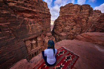 Woman traveler sitting on viewpoint in Petra ancient city looking at Treasury Al-khazneh.
