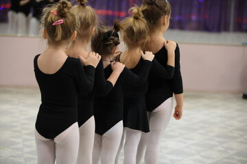 A group of little girls in sporty black swimsuits dancing in the gym standing together in a row at a ballet school class