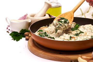 Delicious small meatballs with spinach in a creamy sauce in the frying pan