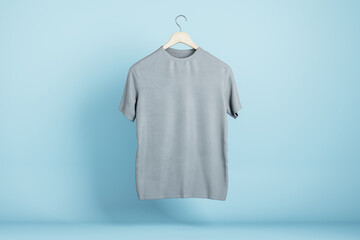 Empty gray tshirt hanging on blue wall background. Product design and presentation concept. Mock up...