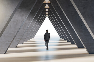 Back view of businessman walking in abstract concrete triangle corridor. Space and hallway concept.