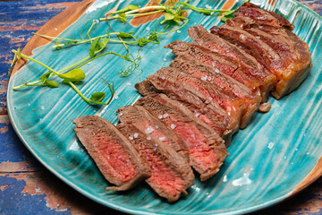 Juicy medium rare beef steak slices on ceramic board with herbs spices and salt.