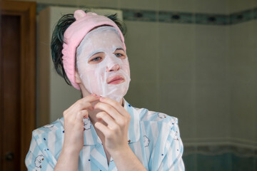 A young girl puts a tissue cosmetic mask on her face. Skin care, lifestyle.