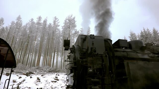 Slow motion of historical steaming black locomotive in front of snow covered forest in Harz mountains, Germany