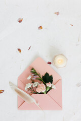 Pink cardboard envelope top view. fresh flowers and a feather are inserted into the envelope. Composition for inscriptions. A burning candle is nearby.