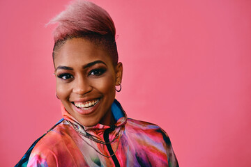 Portrait of a happy stylish young woman with pink hair and colorful fashion jacket on pink background