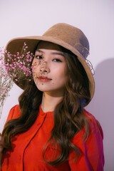 young asian woman in straw hat, smiling and holding flowers isolated on pink