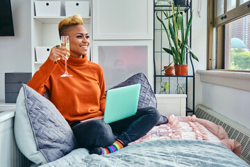 Young woman celebrating with champagne at home during video call on laptop at home