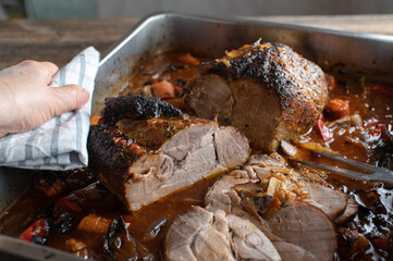 Fresh cooked roasted pork with gravy in a roasting pan is being held by a womans hand