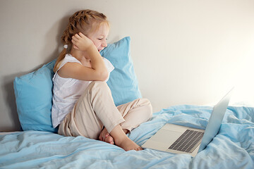 A cute girl sitting on the bed is watching something on a laptop. The concept of education.