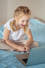 A cute girl sitting on the bed is watching something on a laptop. The concept of education.