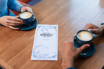 partial view of couple near coffee cups and menu on table