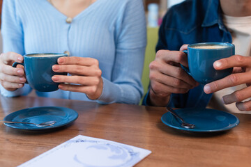 cropped view of blurred couple holding coffee cups near menu on restaurant table