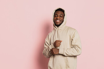 Smiling guy, young dark skinned man wearing hoodie, youth clothes isolated on pink studio background with copyspace for ad.
