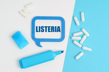 On a white and blue table are pills, a marker and a blue plaque with the inscription - Listeria