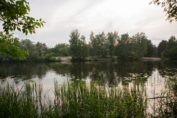 Beautiful nature with pond lake, green trees foliage, grass and  clouds in the background. Afternoon panorama landscape at Pokrovskoe Streshnevo urban forest park, Moscow, Russia