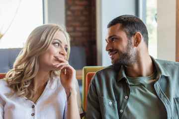 Naklejka premium pleased couple smiling at each other while sitting in cafe