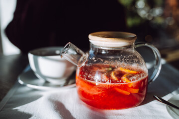 Unrecognizable woman sit in cafe with glass pot of hot winter tea by table with white tablecloth.