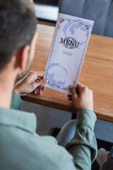 cropped view of blurred man holding menu in restaurant