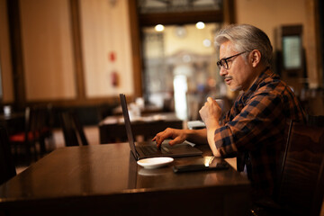 Businessman working on laptop in cafe. Handsome senior man enjoying in fresh coffee.