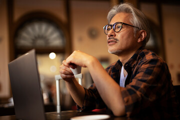 Businessman working on laptop in cafe. Handsome senior man enjoying in fresh coffee.