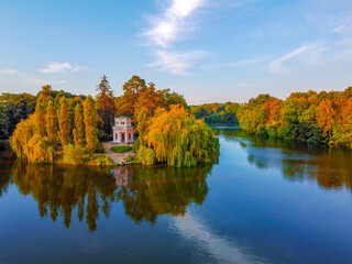 Obraz premium An island with a gazebo in the middle of the lake, autumn landscape, yellowed leaves of trees lake and blue sky.