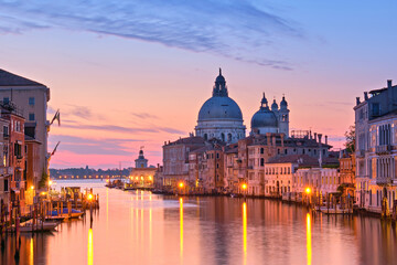 Romantic Venice at dawn, sunrise. Cityscape image of Grand Canal in Venice, with Santa Maria della Salute Basilica reflected in calm sea. Street lights reflected in calm water. - obrazy, fototapety, plakaty