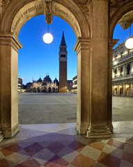 Doge Palace in Venice, Campanile tower and basilica on Piazza di San Marco visible through ancient arch with circle street lamp. Romantic evening, night in Venice, Italy. Center of town at dawn.