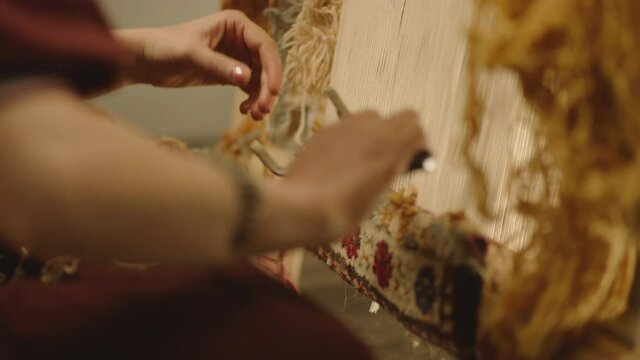 A Woman weaving traditional Asian carpet . Handmade carpet embroidery . Women 's hands create a pattern using multi-colored threads . Close up view . Weaving machine . Needlework . Carpet-makers 
