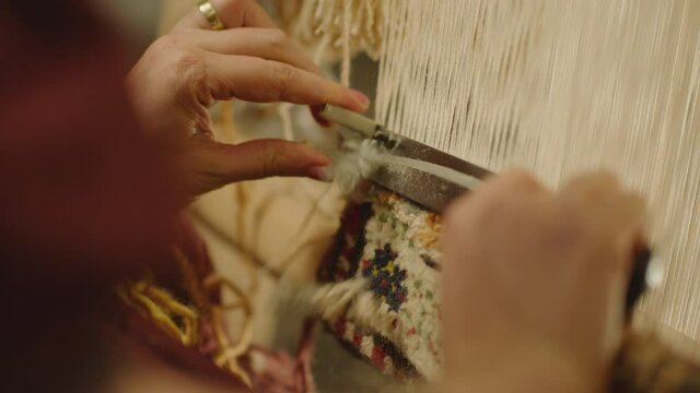 A Woman weaving traditional Asian carpet . Handmade carpet embroidery . Women 's hands create a pattern using multi-colored threads . Close up view . Weaving machine . Needlework . Carpet-makers 