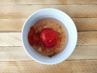 Pickled tomatoes with garlic in a plate on a wooden background