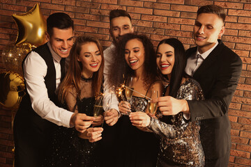 Happy friends with glasses of sparkling wine and sparklers celebrating New Year indoors