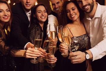 Happy friends celebrating New Year indoors, focus on hands with glasses of sparkling wine