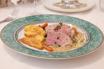Close up of a plate of roasted pork tenderloin slices beside with pan-fried apple pieces and baby carrots, mustard sauce topped with baby bean sprout and thyme leaves