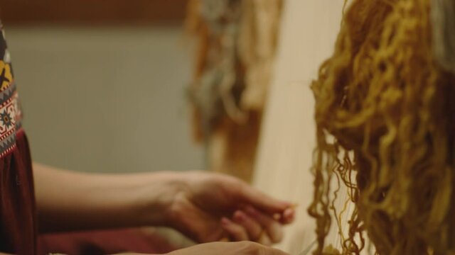 A Woman weaving traditional Asian carpet . Handmade carpet embroidery . Women 's hands create a pattern using multi-colored threads . Close up view . Weaving machine . Needlework . Carpet-makers 