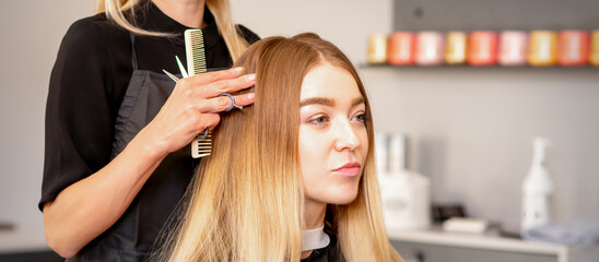 Gorgeous blonde long hair woman and her hairdresser looking and checking out hairstyle. Beautiful hairstyle of a young blonde woman after dying hair in a beauty salon, results of hair treatment