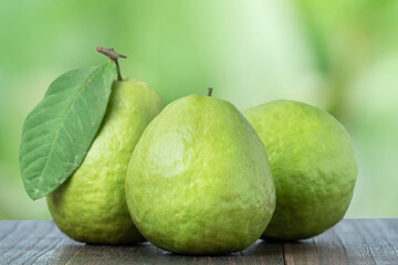 Delicious guava with fresh green leaves on wooden table and green nature background.