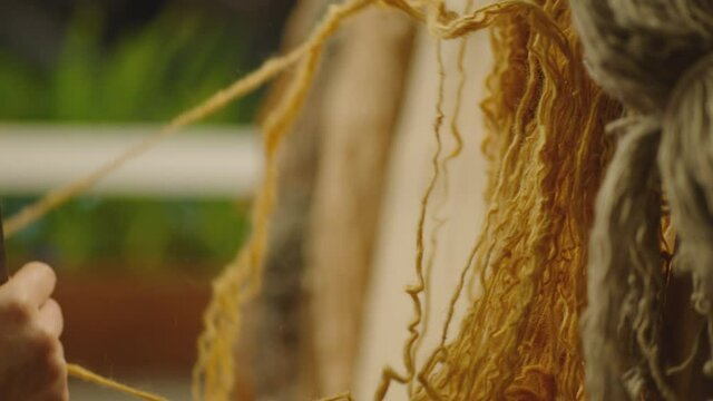 A Woman weaving traditional Asian carpet . Handmade carpet embroidery . Women 's hands create a pattern using multi-colored threads . Close up view . Weaving machine . Needlework . Carpet-makers 