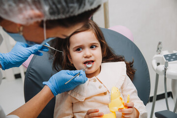 dentist, doctor examines the oral cavity of a little girl, uses a mouth mirror, baby teeth...