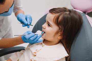 dentist, doctor examines the oral cavity of a little girl, uses a mouth mirror, baby teeth...