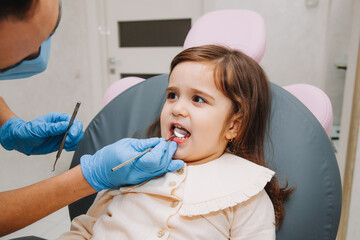 dentist, doctor examines the oral cavity of a little girl, uses a mouth mirror, baby teeth...