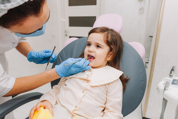 dentist, doctor examines the oral cavity of a little girl, uses a mouth mirror, baby teeth...