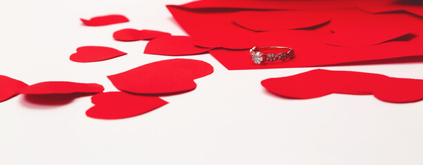 Marry me concept, wedding engagement ring with with red paper envelope and paper hearts on white background. Happy valentines day present. Close up, copy space,