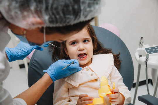 dentist, doctor examines the oral cavity of a little girl, uses a mouth mirror, baby teeth close-up, the concept of pediatric dentistry, dental treatment.