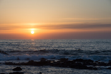 水平線に沈む夕陽と岩の海岸
