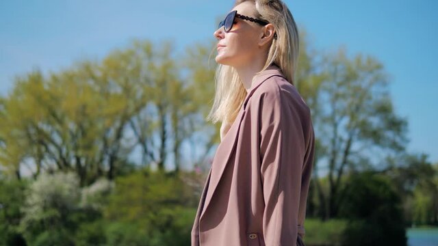 beautiful blonde girl in sunglasses walks through the park and straightens her hair