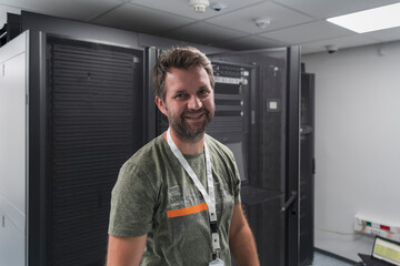 Portrait of male technician or network administrator standing brave as a hero with arms crossed in data center server room.